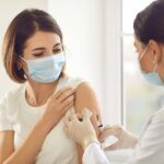 Young woman in medical face mask getting Covid-19 vaccine at doctor's office.